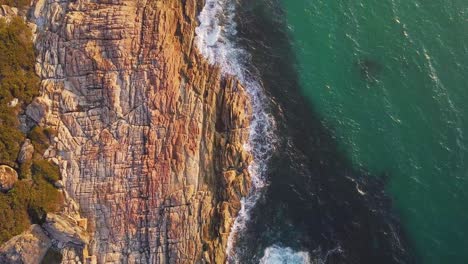 Top-down-view-of-a-waves-crashing-on-the-rocky-coast-in-Western-Australia-during-sunrise-with-soft-morning-light