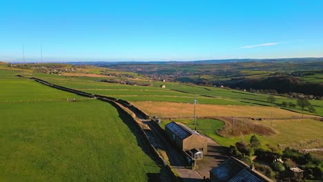 Aerial-drone-video-footage-of-English-farmland-showing-green-fields,-patchwork-landscape,-hills-and-a-farmhouse-in-a-rural-setting