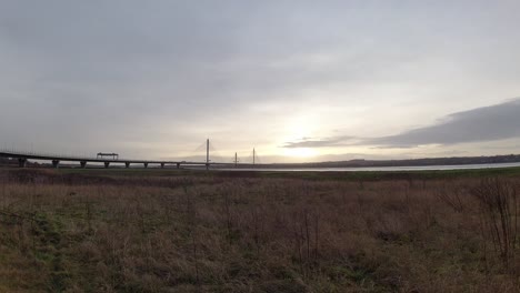 Morning-sunrise-traffic-commuters-driving-timelapse-over-transport-bridge-crossing-over-grassland-marsh