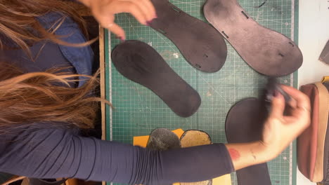 Vertical-time-lapse-female-shoemaker-brushing-stain-onto-sole-shaped-pieces-in-workshop