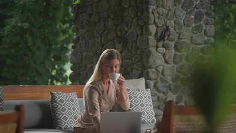 Fokussierte-Geschäftsfrau,-Die-Am-Laptop-In-Der-Bali-Resort-Lounge-Arbeitet,-Während-Sie-Kaffee-Trinkt