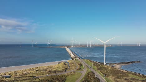 Aerial-slow-motion-shot-of-wind-turbines-and-a-road-in-a-coastal-area-of-the-Netherlands-on-a-beautiful-sunny-day