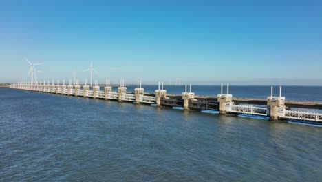 Aerial-slow-motion-shot-of-the-Eastern-Scheldt-storm-surge-barrier-and-wind-turbines-in-the-distance-in-Zeeland,-the-Netherlands-on-a-beautiful-sunny-day