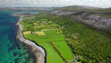 Small-road-through-rural-landscape-and-coastline-in-West-Ireland,-forward-aerial