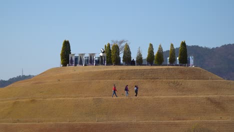 Group-of-People-walking-up-the-Bonghwa-Hill-on-a-spiral-footpath-in-Lake-Garden-of-Suncheonman-Bay-National-Garden,-South-Korea---Static-skyline