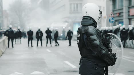 Cinematic-shot-of-unrecognizable-police-officer-in-full-gear-protecting-the-street-with-his-unit-during-riots