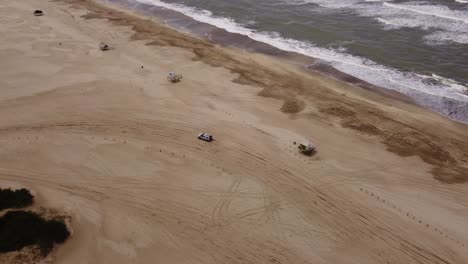 Aerial-view-of-four-wheel-car-driving-on-sandy-beach-during-sunny-day-in-summer,tracking-shot
