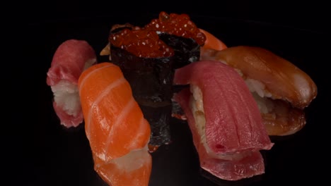 Macro-view-turning-nigiri-sushi-selection-on-black-reflective-glass-background-with-toro-tuna,-salmon,-lemon-fish,-salmon-roe-and-bbq-eel,-Japanese-cuisine-seafood-4K-shot