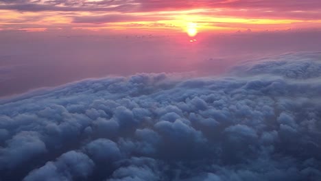 Fliegen-über-Wolken-Und-Einem-Meer-Darunter-Mit-Einem-Farbenprächtigen-Sonnenuntergang-Am-Horizont