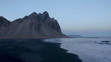 Aerial-forward-flight-over-volcanic-black-beach-and-Vestrahorn-Mountain-in-background---Early-morning-on-Iceland-Island