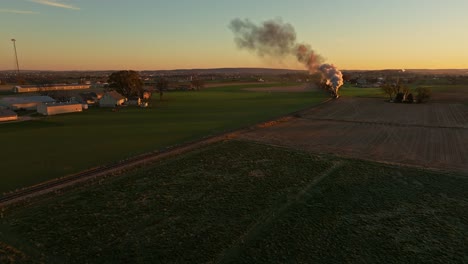 Drohnenansicht-Einer-Dampfmaschine,-Die-Sich-Nähert-Und-Bei-Sonnenaufgang-Rauch-Durch-Das-Ackerland-Am-Herbstmorgen-Fährt