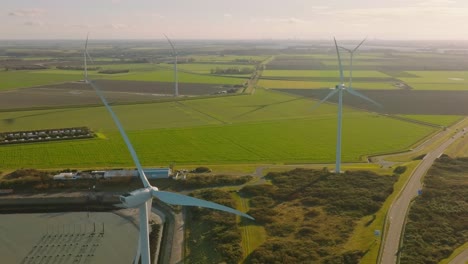 Aerial-slow-motion-shot-of-wind-turbines-and-traffic-on-a-road-in-a-rural-area-of-the-Netherlands-on-a-beautiful-sunny-day-around-sunset