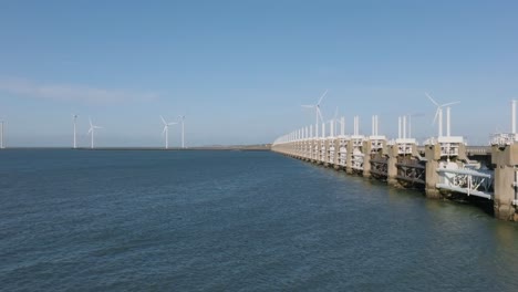 Aerial-slow-motion-shot-of-the-Eastern-Scheldt-storm-surge-barrier-and-wind-turbines-on-a-beautiful-sunny-day-with-a-blue-sky