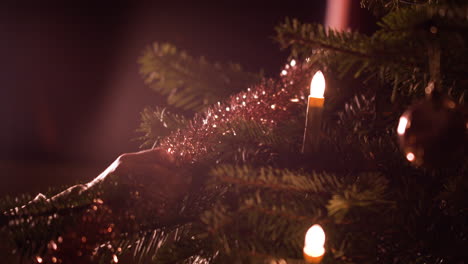 Close-up,-woman's-hands-hanging-up-tinsel-decoration-onto-Christmas-tree-at-home