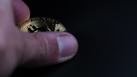 Eine-Männliche-Hand,-Die-Goldenes-Bitcoin-Von-Einem-Dunklen-Hintergrund-Aufhebt