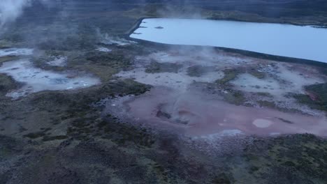 Aerial-tilt-down-shot-of-volcanic-geothermal-landscape-with-boiling-crater-mud-pots-during-cloudy-day-in-Iceland,Europe