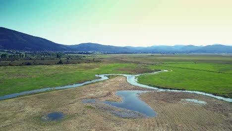 Wide-angle-Dolly-in-drone-shot-of-Lake-Cerknica-flowing-path-and-surrounding-Hills-during-the-day