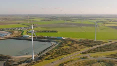 Aerial-slow-motion-shot-of-wind-turbines-and-a-road-in-a-rural,-coastal-area-of-the-Netherlands-on-a-beautiful-sunny-day