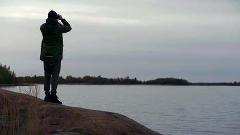 Behind-man-standing-at-lake-looking-through-binoculars,-Looing-over-lake