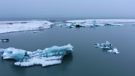 Toma-Aérea-De-Drones-Del-Lago-Glaciar-Islandés-Con-Icebergs-Nevados-Durante-La-Nube-Gris-En-El-Cielo---Jo-Kulsa-Rlo-N-En-Islandia---Concepto-De-Calentamiento-Global