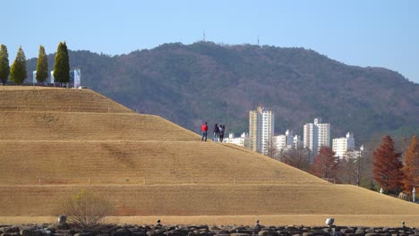 Visitors-strolling-up-the-Bonghwa-Hill-on-a-spiral-road-in-Lake-Garden-of-Suncheonman-Bay-National-Garden-with-Suncheon-city-buildings-and-mountains-on-background