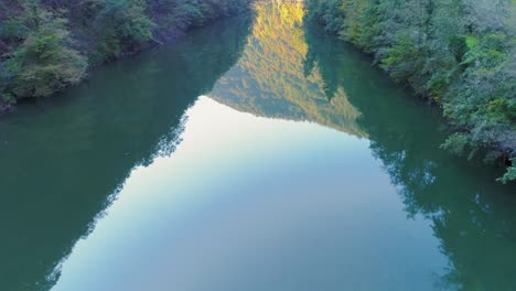 Aerial-shot-of-a-mountain-and-forest-reflecting-on-Kolpa-river-surface-near-Kostel,-Slovenia