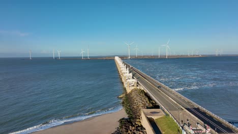 Aerial-slow-motion-shot-of-sparse-traffic-on-the-open-Eastern-Scheldt-storm-surge-barrier-and-wind-turbines-in-Zeeland,-the-Netherlands-on-a-beautiful-sunny-day