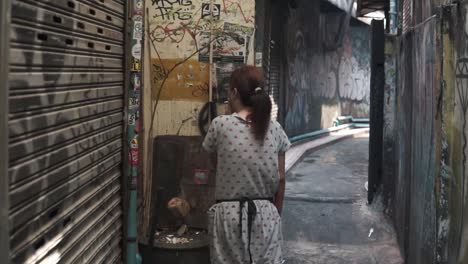 Movement----Lonely-asian-thai-woman-smoking-a-cigarette-looking-at-paintings-at-the-wall-in-narrow-alley-in-Bangkok,-Thailand----Stabilized-gimbal-shot-passing-woman----Full-HD-wide-angle-shot