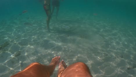 Underwater-personal-perspective-view-of-man-legs-floating-in-clear-transparent-sea-water,-slow-motion