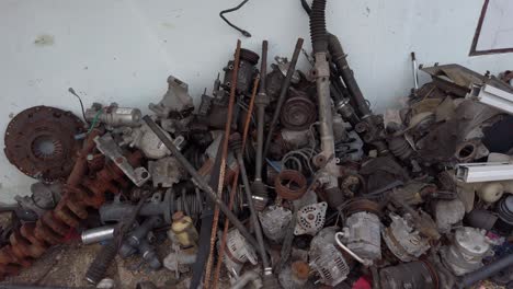 Pan-shot-of-pile-of-junk-metal-machine-parts-mess-against-white-wall