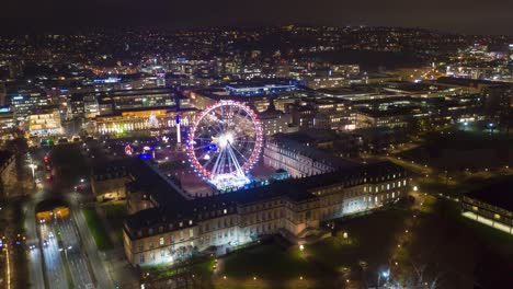 Moving-aerial-night-time-lapse-in-4k-of-downtown-skyline-in-the-city-of-Stuttgart,-Germany-with-Schlossplatz,-the-Länd-ferris-wheel-and-christmas-market