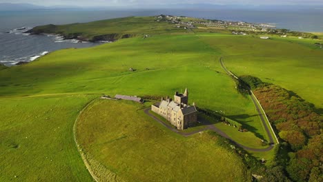 Classiebawn-Castle-in-scenic-rural-coastal-landscape-in-Ireland,-pullback-aerial