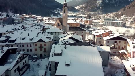 Pellizzano-winter-scene,-small-mountain-village-church-covered-in-snow,-aerial-reveal