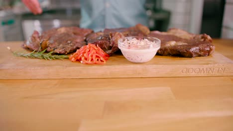 Man-with-a-grilled-marinated-beef-flank-steak-on-a-wooden-board-placed-on-the-table-ready-to-serve