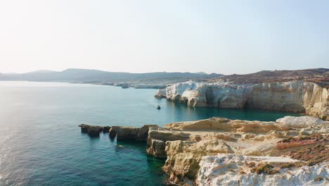 Sarakiniko-Beach-coastline-with-a-boat-sailing-the-mediterranean-sea-in-Milos-greek-island,-drone-shot-dolly-in