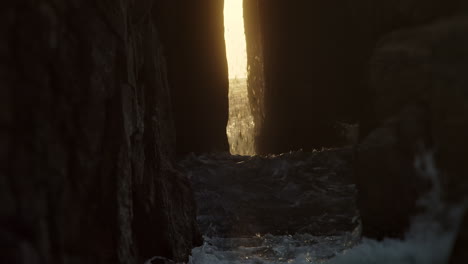 Gold-Sunset-Sunlight-Ray-Shining-through-Cave-Passage-as-Ocean-Waves-Crash-Nanjjizal,-Cornwall
