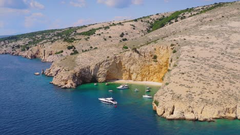 Cliffed-coast-of-Croatian-island-Krk-with-secluded-sandy-beach-Golden-Bay-and-luxury-yachts-floating-in-the-calm-lagoon