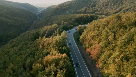 Aerial-tilt-up-view-drone-shot-of-cars-driving-on-a-winding-mountain-road-in-the-middle-of-an-autumn-coloured-forest