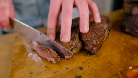 Close-up-view-of-Male-hand-with-a-knife-slicing-the-juicy-grilled-Beef-Steak-on-cutting-Board