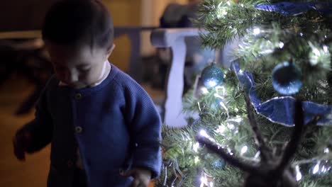 Lindo-Bebé-Latino-Caminando-Hacia-El-árbol-De-Navidad-Para-Colocar-Una-Burbuja-Azul