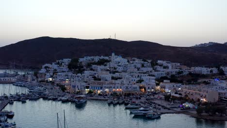 Aerial-view-of-Adamantas-port-town-in-Milos-greek-island,-nightfall-drone-dolly-out