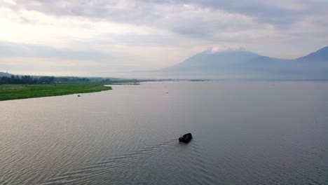 Aerial-view-following-fishing-boat-motoring-along-lake-coast-in-Indonesia-4K