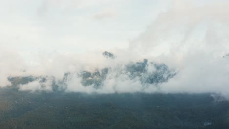 Opening-aerial-drone-shot-of-a-green-forest-covered-mountain,-flying-through-light-wispy-clouds