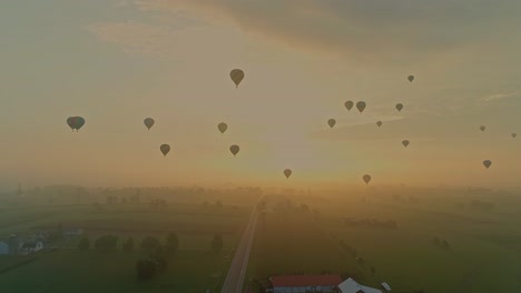 An-Aerial-View-of-Multiple-Hot-Air-Balloons-Floating-into-the-Early-Mist-With-a-Red-Sun-During-a-Festival-With-Crowds-Watching,-on-a-Summer-Day