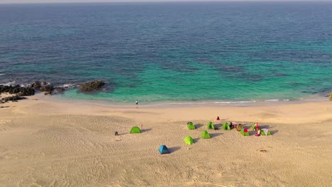 Aerial-view-of-travelers-camped-on-a-beach-in-Oman,-with-tents-and-utility-vehicles