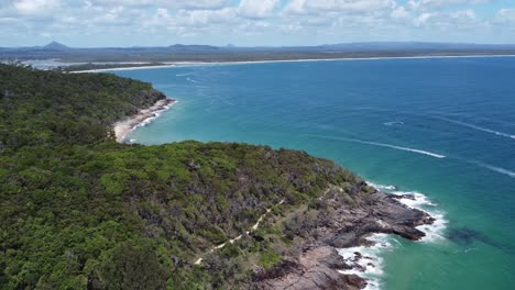 Drone-descending-over-a-peninsula-showing-rocky-beach-below