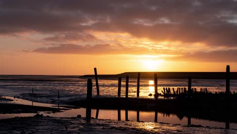 Sunrise-time-lapse-over-mudflats,-ocean-and-shoreline-with-wooden-poles-at-texel-Frisian-wadden-island