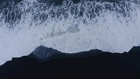 Powerful-Atlantic-waves-rolling-in-on-black-sand-beach-in-Iceland---aerial-ascending-straight-down