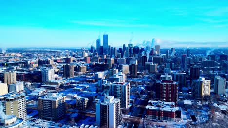 buttery-smooth-aerial-reverse-flyover-downtown-capitol-city-of-Edmonton-from-North-East-to-North-West-snow-covered-buildings-are-steaming-thru-chimney's-during-extreme-cold-weather-skyline-view2-2