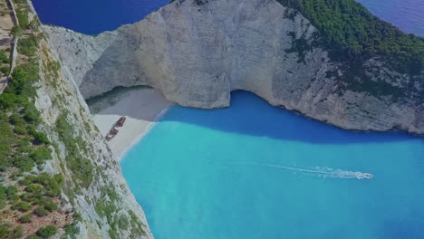 Aerial-over-boat-in-Zakynthos-Greece-Navagio-Shipwreck-cove-with-blue-water